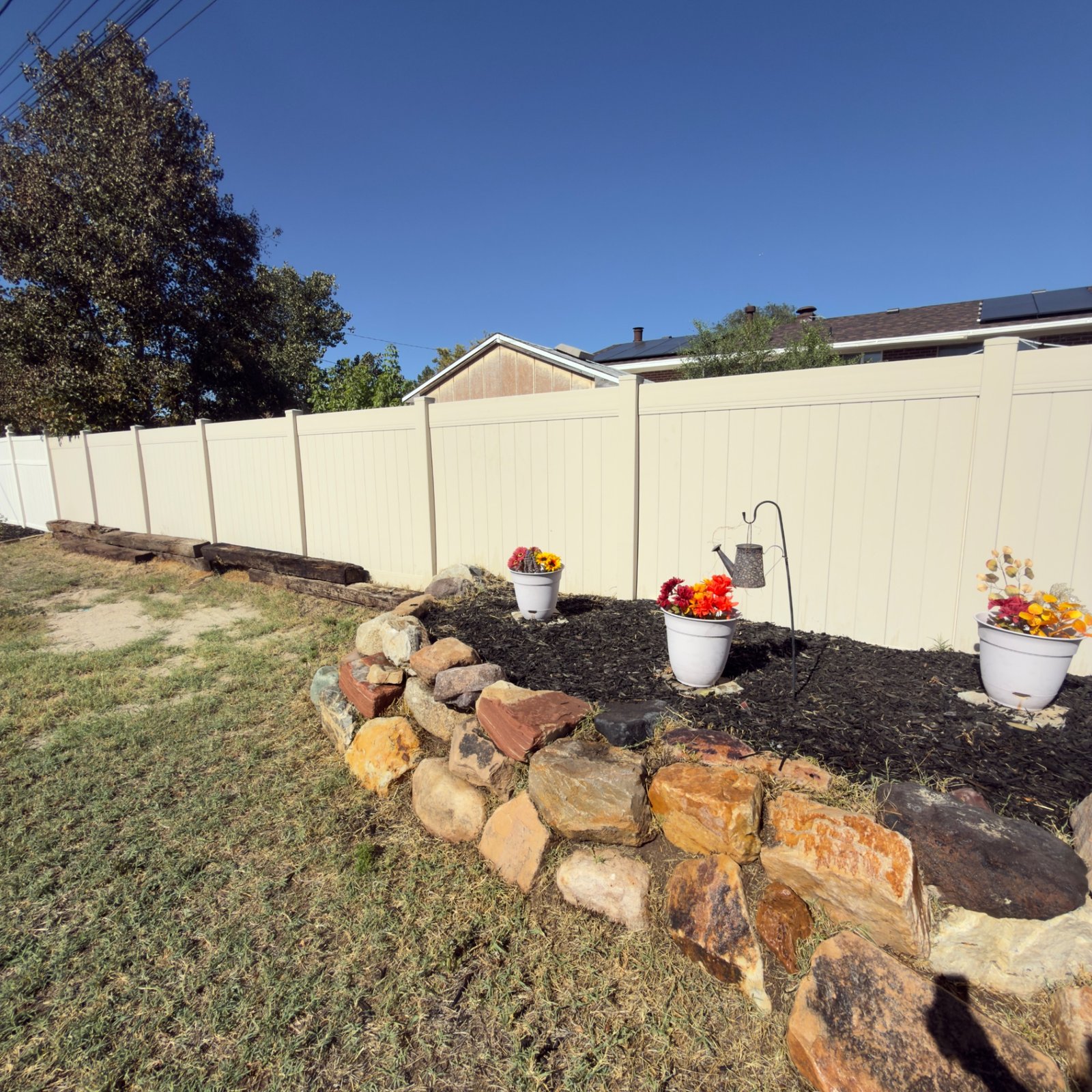 Row of colorful flower planters and a watering-can garden accent along the vinyl fence